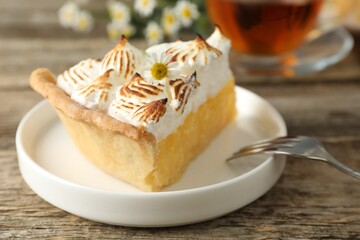 Piece of delicious pie with browned meringue and fork on wooden table, closeup