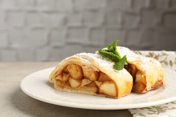 Pieces of tasty apple strudel with powdered sugar and mint on grey textured table, closeup