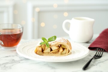 Piece of tasty apple strudel served with tea on white marble table, closeup