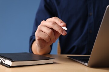 Man with pen working on laptop at desk against blue background, closeup
