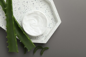 Moisturizing cream with extract of aloe vera in jar and cut leaves on grey background, flat lay. Space for text