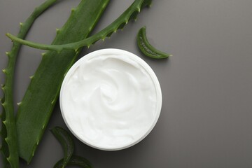 Moisturizing cream with extract of aloe vera in jar and cut leaves on grey background, flat lay. Space for text