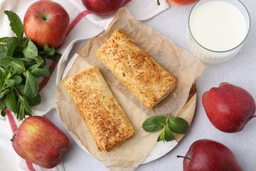 Tasty apple strudels, mint, fruits and milk on light table, flat lay