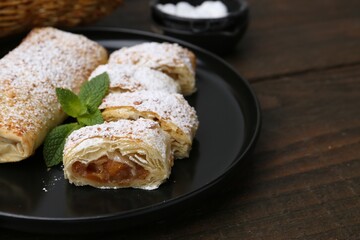 Tasty apple strudels with powdered sugar and mint on wooden table, closeup. Space for text