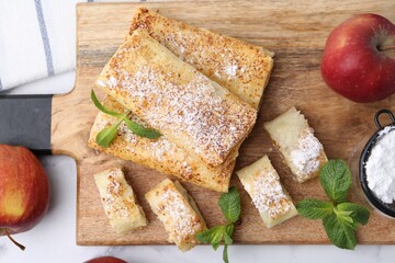 Tasty apple strudels with powdered sugar, fruits and mint on white table, flat lay