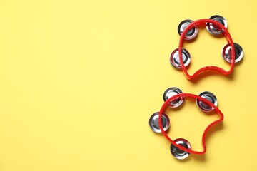 Bright toy tambourines on yellow background, flat lay. Space for text