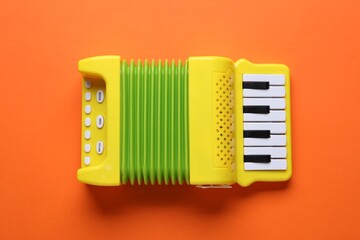 Toy accordion on orange background, top view. Child's musical instrument