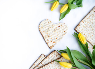 Layout of Traditional Matzah shape of heart prepared for Passover with on white background with yellow tulips and ribbon. banner. top view. Spring Holiday of Jewish people. Fasting time