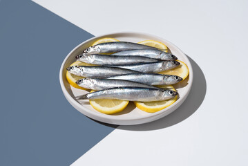 Anchoas frescas sobre rodajas de limón dentro de un plato sobre fondo blanco y azul