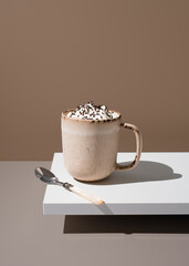 Caf&eacute; servido en taza con crema de leche y fideos de chocolate sobre fondo marr&oacute;n