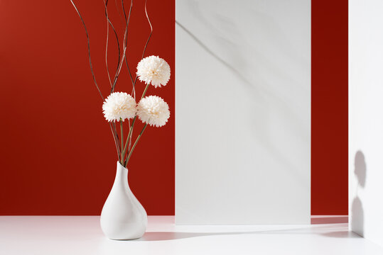 Flores de crisantemo blancas decorativas en un jarr&oacute;n blanco sobre fondo rojo	