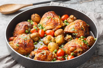Honey garlic chicken thighs baked with mushrooms, green peas, cherry tomatoes and herbs close-up in a frying pan on the table. Horizontal