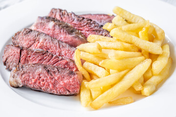 Sliced Medium-Rare Ribeye Steak with French Fries on White Plate