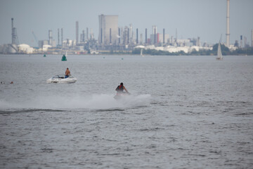 Jet skier performs tricks near industrial skyline along the waterfront on a clear day