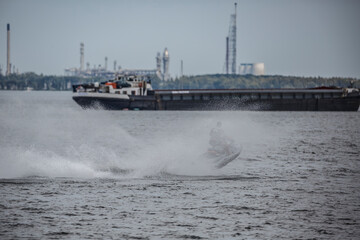 Watercraft performs thrilling jump over waves near industrial landscape at dusk