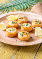Fried scallops with butter, lemon, parsley on rustic yellow wooden table