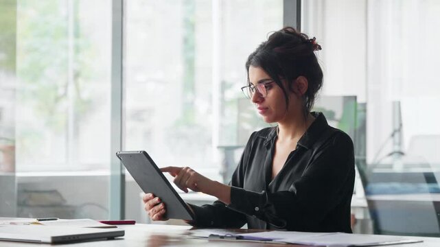 Smiling latina young professional business woman looking at pc device computer screen. Indian female businesswoman specialist holding digital tablet, using tab pad financial app at work in office