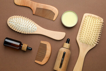 Wooden hair brushes, combs and cosmetic products on dark beige background, flat lay
