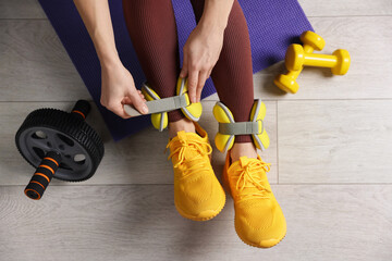 Woman putting on ankle weights and gym equipment indoors, top view