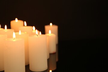 Many burning candles in darkness, closeup. Space for text