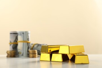 Shiny gold bars and money on beige background, selective focus. Space for text