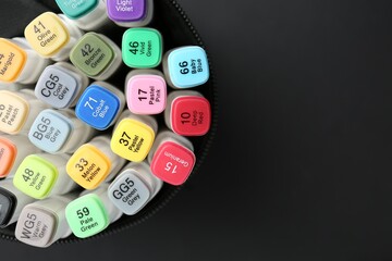 Many colorful marker pens in holder on black background, top view. Space for text