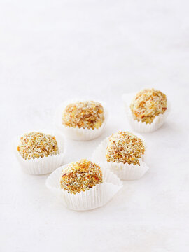 Small, round dessert balls are arranged artistically on a light surface, each encased in a delicate white wrapper. Their golden crust gleams invitingly, promising sweet flavors