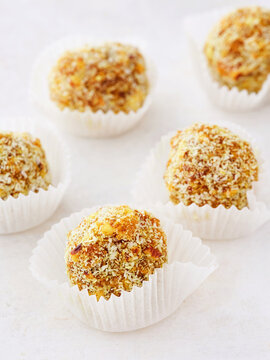 Small, round dessert balls are arranged artistically on a light surface, each encased in a delicate white wrapper. Their golden crust gleams invitingly, promising sweet flavors