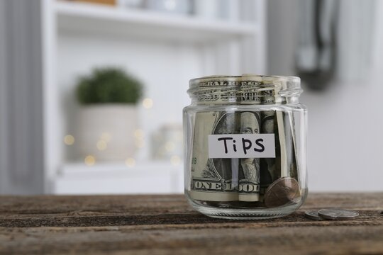 Glass jar with tips on wooden table indoors, space for text