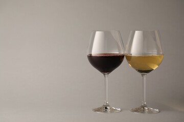 Red and white wine in glasses on light grey background, space for text