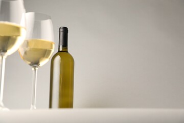 Tasty white wine in glasses and bottle on light grey background, low angle view. Space for text