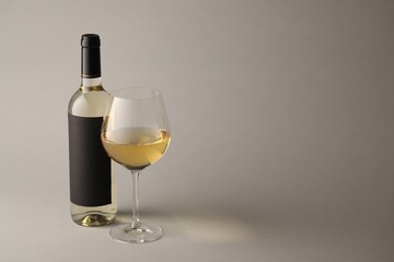 Tasty white wine in glass and bottle on light grey background, space for text