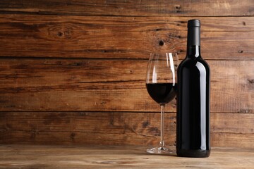 Tasty red wine in glass and bottle on wooden table, space for text