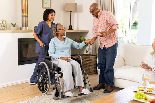 Elderly man helping woman in wheelchair while caregiver smiling at home