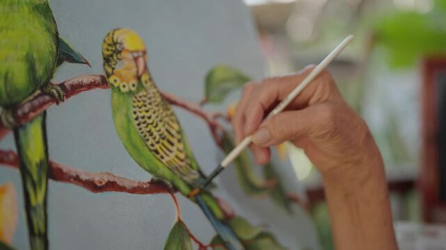 Close up hand of a elderly woman artist painted watercolor of a lively bird on canvases on an wooden easel. Exquisite hand painted watercolor, Showcasing nature inspired artwork