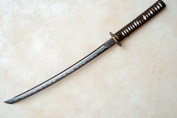 A Japanese sword lies on a textured neutral colored surface
