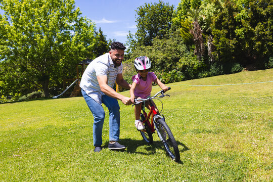 Father teaching daughter to ride bicycle on sunny day in park
