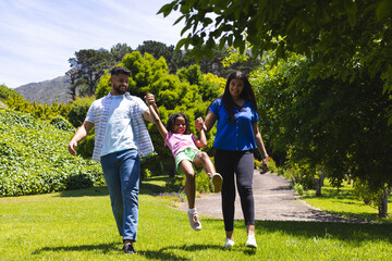 Parents joyfully swinging daughter between them while walking in sunny park