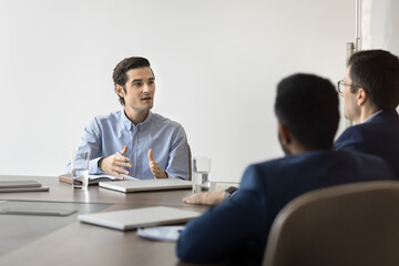 Hispanic boss hold negotiations with investors or shareholders seated at conference table. Staff members engaged in briefing event in company boardroom, analyzing sales data, discuss business strategy