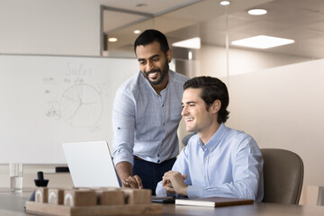 Two positive teammates using laptop in meeting room. Male mentor showing to apprentice new AI...
