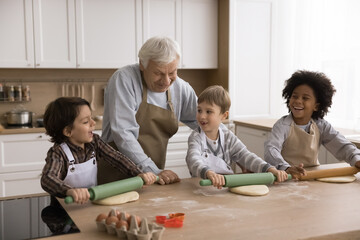 Little chefs. Caring old age grandpa help three multiracial grandchildren school age boys in aprons...