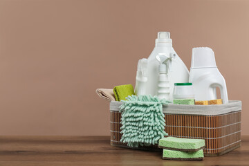Eco-friendly cleaning products and supplies in wicker basket on wooden table against beige background, space for text