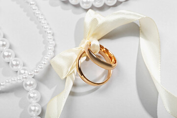 Golden wedding rings tied with ribbon and pearl necklaces on white background, flat lay