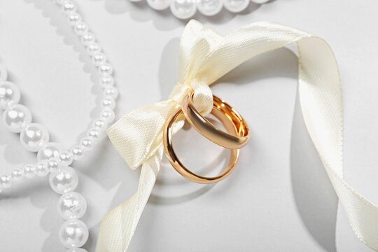 Golden wedding rings tied with ribbon and pearl necklaces on white background, flat lay