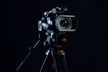 Modern video camera with tripod on black background