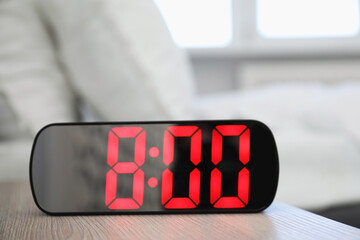 Digital alarm clock showing 8:00 o'clock on bedside table indoors