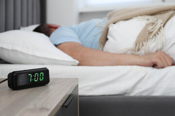 Man sleeping in bed at home, focus on digital alarm