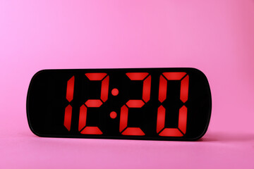 Digital alarm clock showing 12:20 o'clock on pink background, closeup