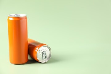 Orange aluminium cans of beverage on pale green background, space for text