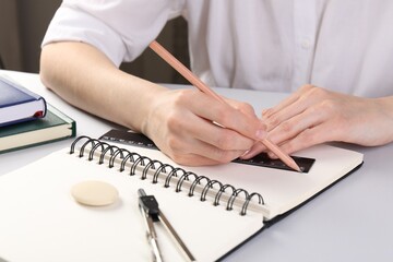 Woman drawing sketch with ruler and pencil on notebook at white table, closeup